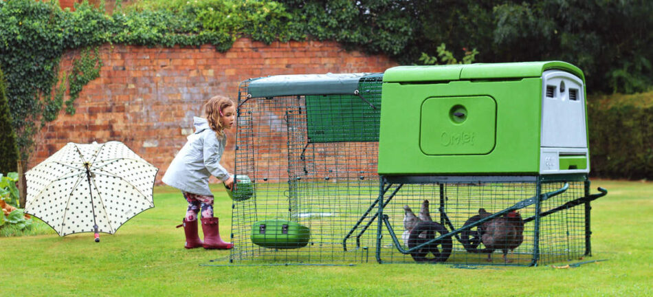 Pige fodrer sine høns i et grønt Eglu Cube hønsehus med løbegård