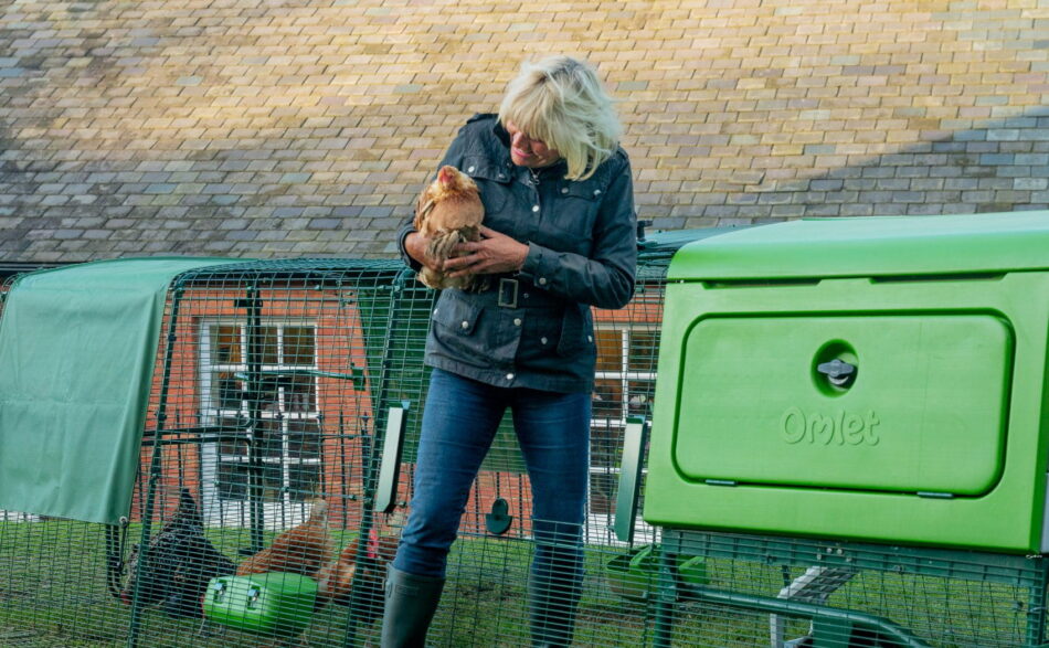 Kvinde, der holder en høne, træder ud af løbegården til Eglu Pro-hønsehuset