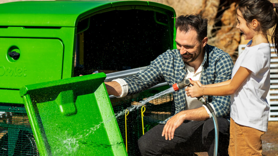 Mand og pige rengør Omlet Eglu Pro-bundbakken med slange